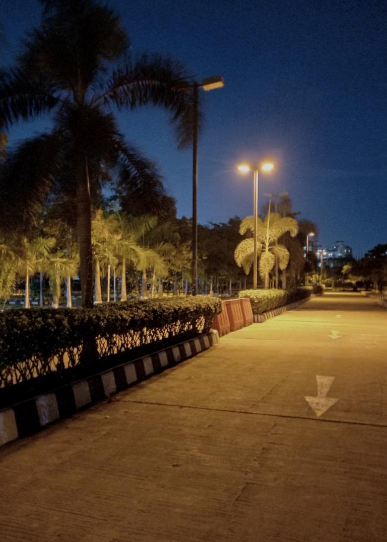 A Dhaka street at dusk under its own lights.